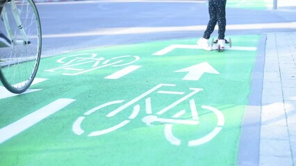 Girl on kick scooter rides on green bike path in city. child on scooter riding in the bike lane. White bicycle sign on green road traffic laws, crosswalk and cars.