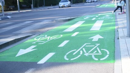 Girl on kick scooter rides on green bike path in city. child on scooter riding in the bike lane. white Bicycle sign on green road traffic laws, crosswalk and cars.