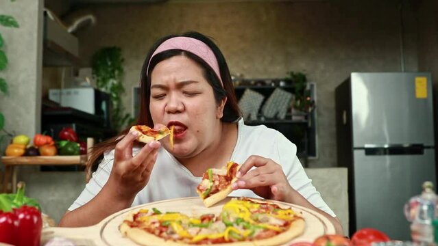 Fat asian happy woman sits and eats her favorite food pizza with great relish greedily overeating causes choking.