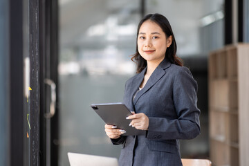 Image of young asian woman, company worker in office, smiling and holding digital tablet, standing over white background blur office