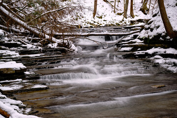 A small waterfall in the forest at Windsor High School in Upstate NY. Stream with snow along the...