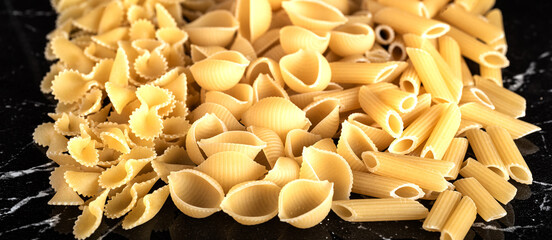 Pasta, capellini, linguini, fettuccine, tagliatelle, papardelle, fusilli, Penne, tortilloni, on a marble surface. Close-up