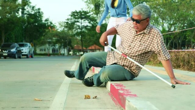 Asian blind old man walking with a cane blind accident accident stumbles on the sidewalk falls down receives first aid help from a kind beautiful woman to get up with concern.