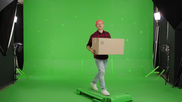 Young casual man walking on a Green Screen, Chroma Key. Man worker holding a box. Delivery concept. Side view