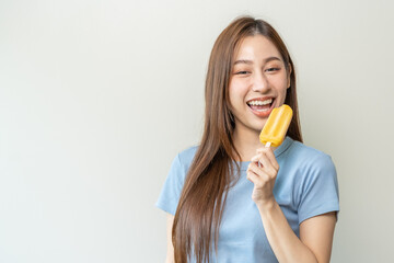 Cheerful enjoy, happy cute asian woman wearing casual with brunette hair, eating popsicle, teenage girl holding ice pop, lolly frozen stick with mango yellow, passion fruit ice cream tasty in summer.