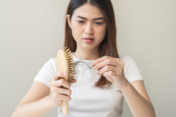 Serious asian young woman holding brush holding comb, hairbrush with fall black hair from scalp...