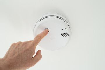 Home owner seen performing a weekly test on a ceiling mounted smoke alarm located in the hall of a...