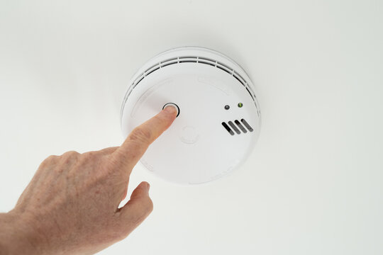 Home owner seen performing a weekly test on a ceiling mounted smoke alarm located in the hall of a house.