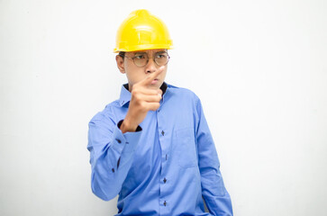asian male construction worker or engineer in blue shirt and safety yellow helmet shows expresion of anger, furious and dissapointment isolated over white. stressed over work concept