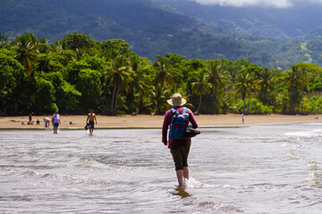 A man wearing a hat and carrying a backpack walks along the beautiful and unique Uvita beach in Marino Ballena National Park in Costa Rica