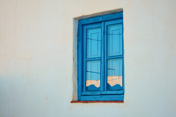 Old blue wooden window with the reflection of the sunset on a white wall