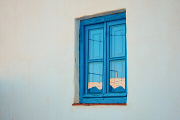 Old blue wooden window with the reflection of the sunset on a white wall