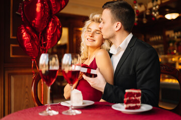 Young couple having a romantic dinner and toasting with glass of red wine. Exchange of gifts. Relationship, surprise and love concept.