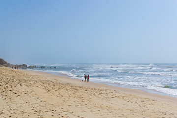 Beach by the ocean with people resting, vacation spot. Mountains, sea and waves. Travel to Europe Portugal.