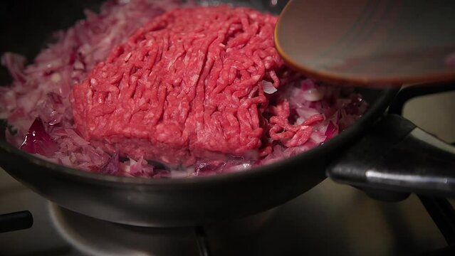 adding raw  ground beef into the frying pan and sauteing it with chopped red onions on the stove