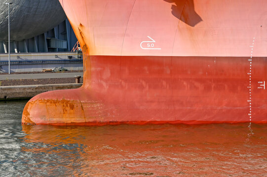 Close up view of the bulbous bow of a large cargo ship with painted markings on the side to indicate its depth in the water. No people.