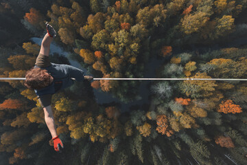Highline over the forest. Rope walker walks on a rope at high altitude. Drone view. Slackline theme - obrazy, fototapety, plakaty