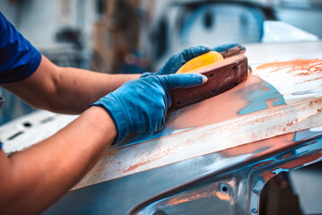 Mechanical repair of body paint. A mechanic repairs a car after an accident. Sand the primer before...