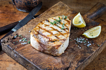Traditional barbecue swordfish steak with salt and lemon served as close-up on an old rustic wooden board - obrazy, fototapety, plakaty