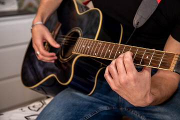 Young man is playing guitar while his girlfriend is singing. Detail of hand on guitar strings.