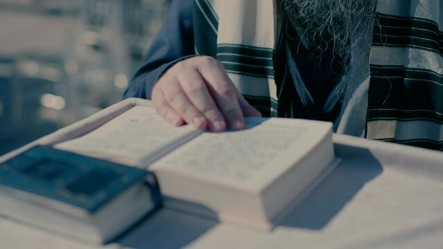 A rabbi with a tallit on his shoulders prays morning prayer with a Torah.