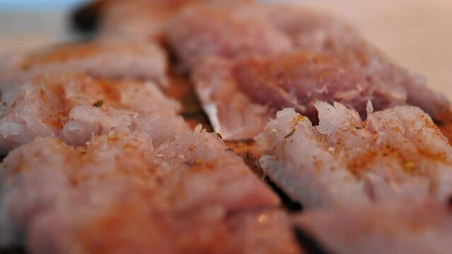 Close-up macro video shooting of a fish fillet. Cook sprinkles raw hake fish with spices while preparing the dish. Cooking fried or baked fish fillet in the home kitchen.