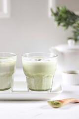 Matcha latte in a transparent glass with milk foam stands on a white background
