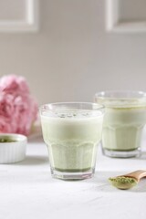Matcha latte in a transparent glass with milk foam stands on a white background

