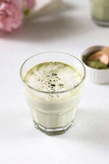 Matcha latte in a transparent glass with milk foam stands on a white background
