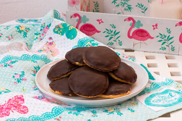 Galletas de chocolate rellenas de mermelada de naranja en un plato blanco, sobre paño de cocina con mariposas y bandeja con flamencos.