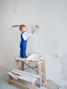 Little boy construction worker painting wall in apartment under renovation. Adorable kid in work overalls using paint roller while playing at future home.