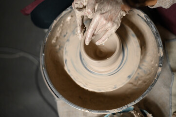 Close-up of a woman beautifully sculpts a brown clay vase on a potter's wheel, a top view