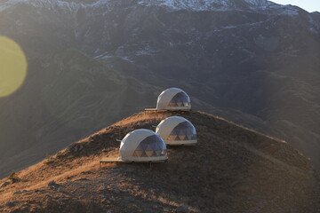 Wavy slopes of mountains overgrown with dry grass and white spherical camping houses - on a sunny winter day in the mountains of Dagestan.