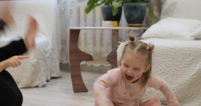 Brother and sister scream and laugh as they roll on the floor in the white living room. The children laugh out loud at the joke and start rolling on the floor. Beautiful children cute show emotions.