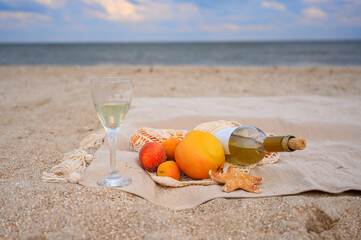 Picnic on the beach. Bottle of wine and fruit on the beach. Glass of wine and seashells. Beach picnic concept. Plaid with fruits on the sandy shore