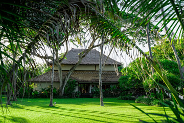 Tropical authentic hotel surrounded by palm greenery stands on the lawn.