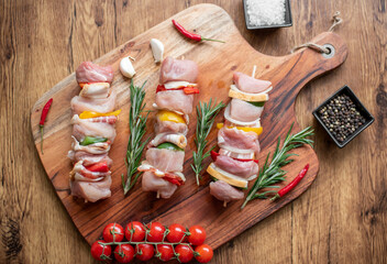 Raw meat skewers with vegetables on wooden background