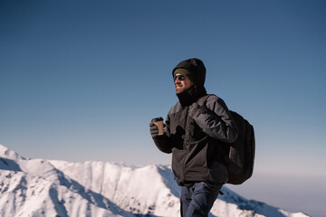 Fototapeta na wymiar a man stands against the background of snow-capped mountains with a paper cup of coffee or tea