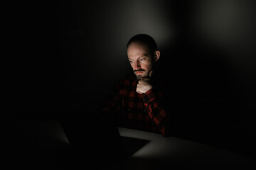 a man carefully looks at a laptop display in total darkness