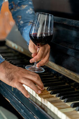 A glass of wine at a man's hand in front of a vintage piano
