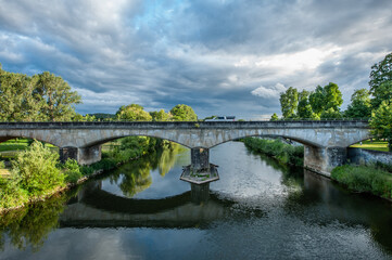 Fototapeta na wymiar Steinbrücke mit Spiegelung in Flusss mit dramatischem Wolkenhimmel