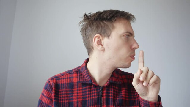 A young man participates in a business meeting online, a video conference via the Internet. A man shows someone behind the scenes a sign to be quiet.