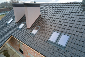 Closeup of attic windows and brick chimneys on house roof top covered with ceramic shingles. Tiled...