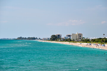 Fototapeta na wymiar Resort beach with white sand, blue water, tall hotel buildings. Happy people sunbathing and swimming in ocean