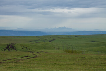 a beautiful landscape in Karachay-Cherkessia with an endless green meadow, a country road and a dramatic sky to the horizon and space to copy