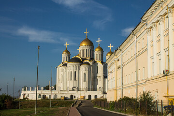 Historical buildings in Vladimir - the white-stone Assumption Cathedral with golden domes and the Museum of Ancient Russian Architecture on a sunny summer day against a blue sky and a space for copy