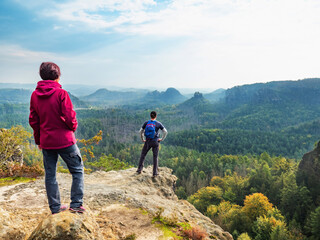 Obraz premium Boy and girl tourists stay on cliff and thinking. Forest in valley with dry spruce trees.