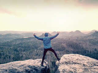 Man in blue sweatshirt with raised arms gesture triumph on exposed cliff