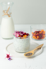 Healthy dessert with yogurt and chia seeds. Berries in a glass and milk in a jug in the background. Vertical view on a light background.