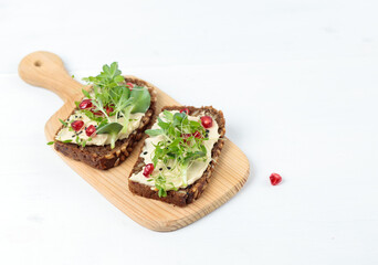 Sandwich with hummus, micro greenery and pomegranate seeds on a wooden board. Close-up on a light background.